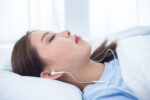 A woman is seen lying in a bed with earphones in her ears.