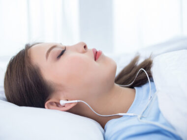 A woman is seen lying in a bed with earphones in her ears.