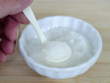 A photograph shows a hand holding a spoonful of salt in a salt cellar.