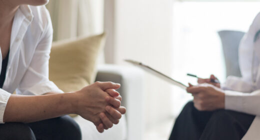 A person sits across from a healthcare professional holding a clipboard during a consultation.