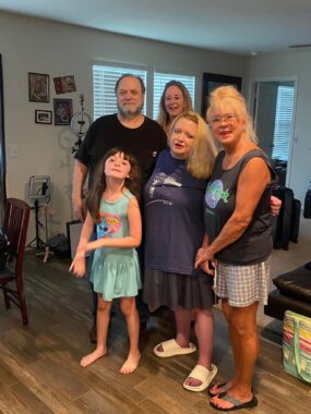 Five family members — four adults and one child — smile for a photo together in what appears to be someone's living room.
