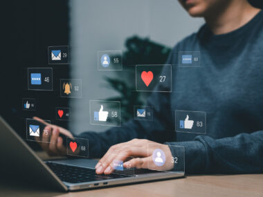 A person is working on a laptop while emojis are shown floating above the keyboard.